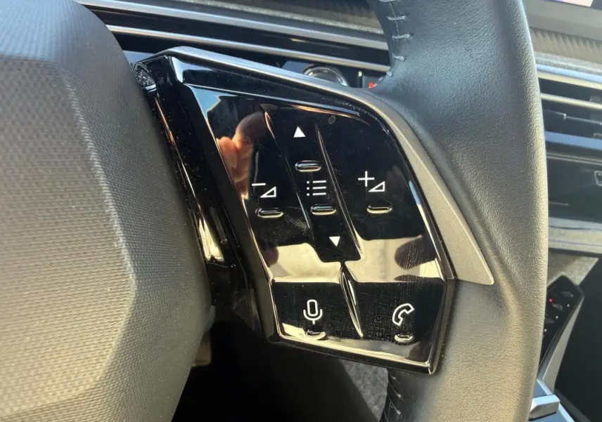 Gros plan sur les commandes tactiles noires à gauche du volant du Peugeot 3008 Hybrid gris, version 2025.