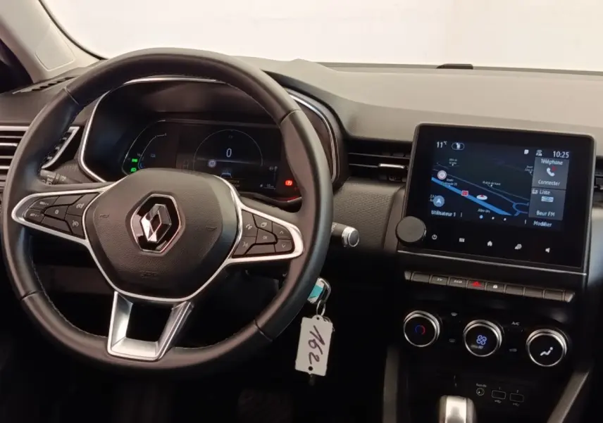 Vue intérieure du tableau de bord de la Renault Clio Business E-TECH 140 avec volant cuir et écran tactile central allumé.