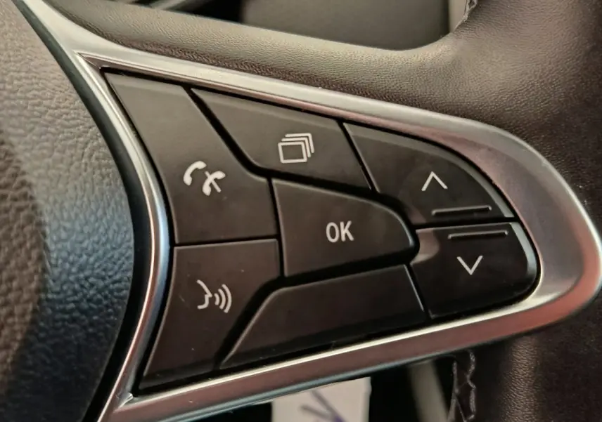 Gros plan sur les commandes multifonctions noires du volant côté gauche de la Renault Clio Business E-TECH blanche.