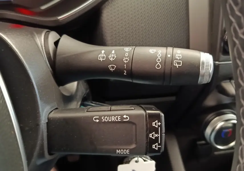 Gros plan sur les commandes au volant noir de la Renault Clio Business E-TECH 140, avec indications blanches et molette argentée.