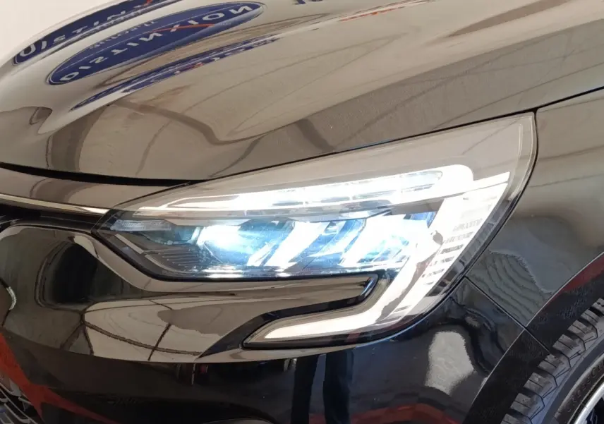 Gros plan sur le phare avant droit allumé d’une Renault Clio noire, soulignant son design LED moderne.