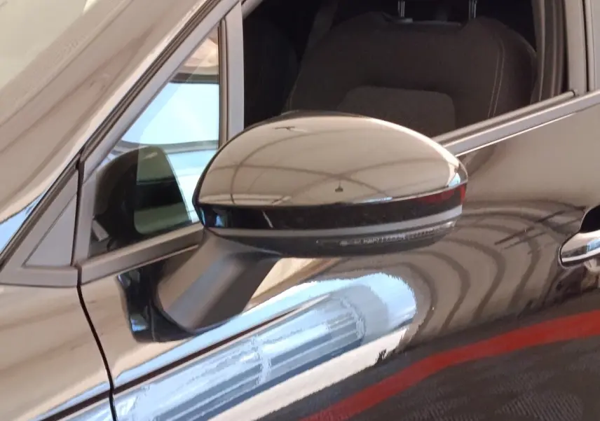 Gros plan sur le rétroviseur droit noir brillant d'une Renault Clio Business E-TECH 140, avec reflet sur la carrosserie noire.