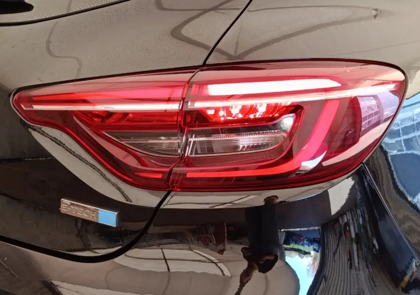 Gros plan sur le feu arrière droit rouge d’une Renault Clio Business E-TECH 140 noire avec badge hybride bleu.