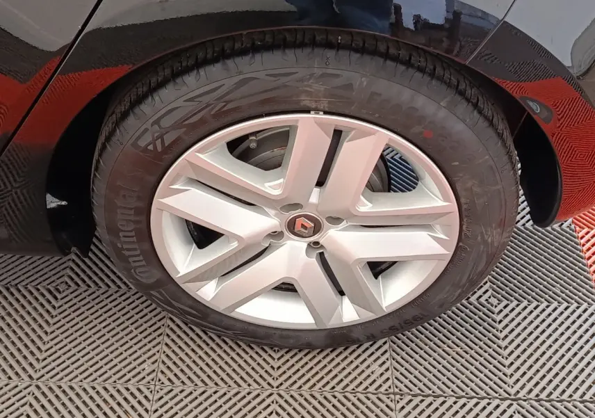 Gros plan sur la roue avant droite d'une Renault Clio blanche, avec jante alliage et logo Renault central visible.