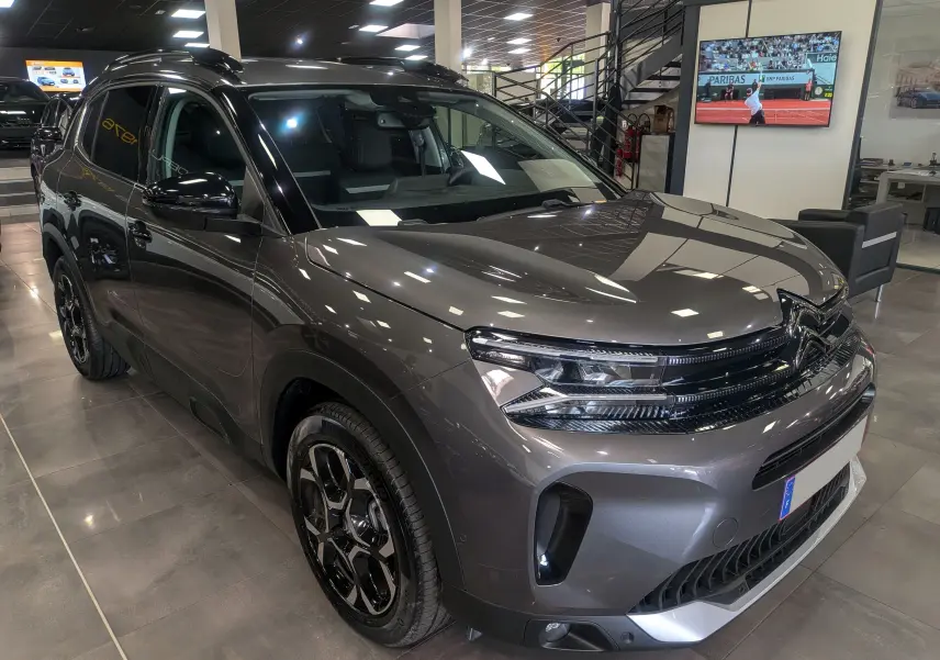 Vue 3/4 avant droite d'un Citroën C5 Aircross Hybride gris Platinium avec jantes noires biton dans un showroom.