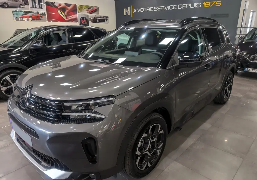 Vue 3/4 avant droite d'un Citroën C5 Aircross hybride gris Platinium avec jantes bi-ton et toit noir en showroom.