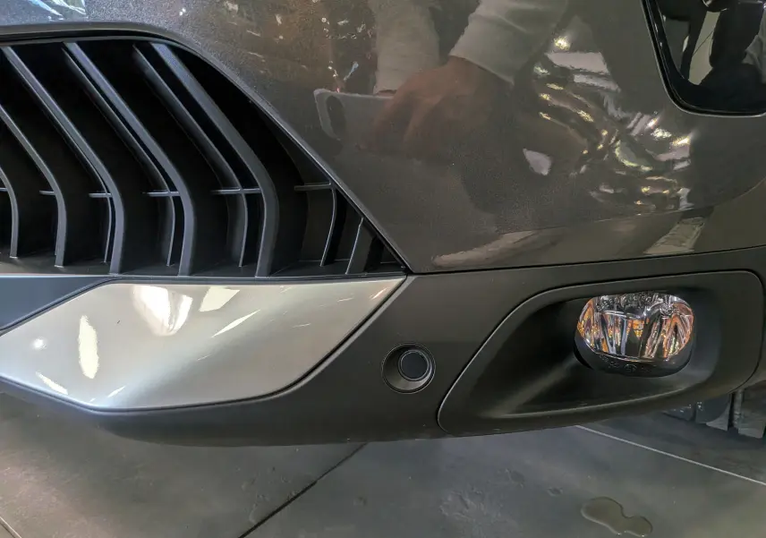 Gros plan sur le pare-chocs avant gris platinium du Citroën C5 Aircross hybride, avec antibrouillard et capteur de stationnement.