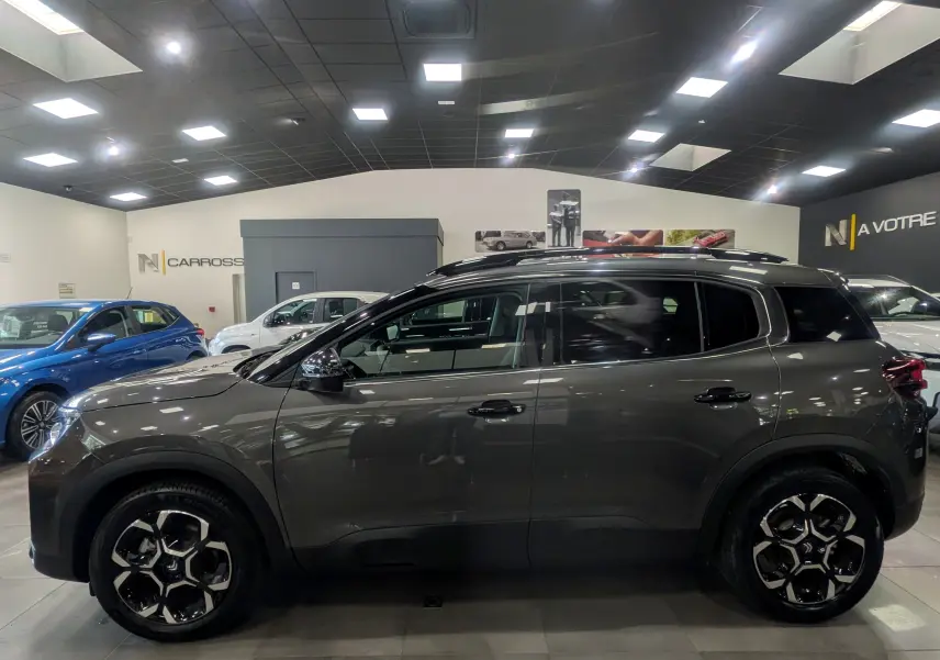 Vue de profil côté gauche du Citroën C5 Aircross Hybride gris Platinium avec jantes bi-ton en showroom.