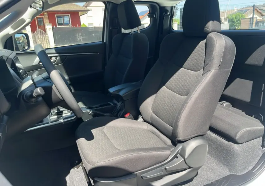 Vue intérieure côté conducteur du pick-up Isuzu D-MAX 2026, sièges tissu gris avec accoudoir central avant.