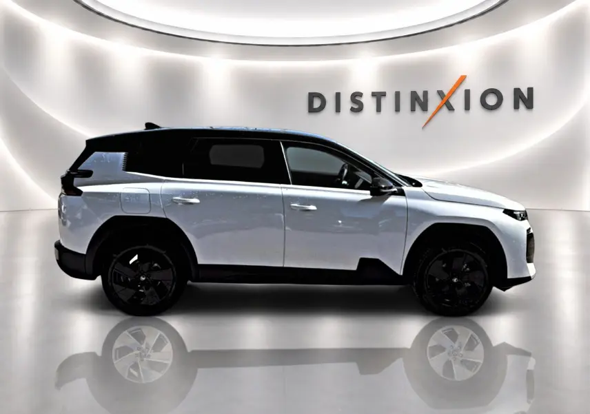 Profil droit du Citroën C5 Aircross hybride 2026 blanc avec toit noir et jantes alliage noires, sur fond lumineux intérieur.
