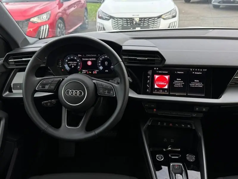 Vue intérieure de l'Audi A3 Sportback blanche 2024, tableau de bord et volant multifonction avec écran digital.