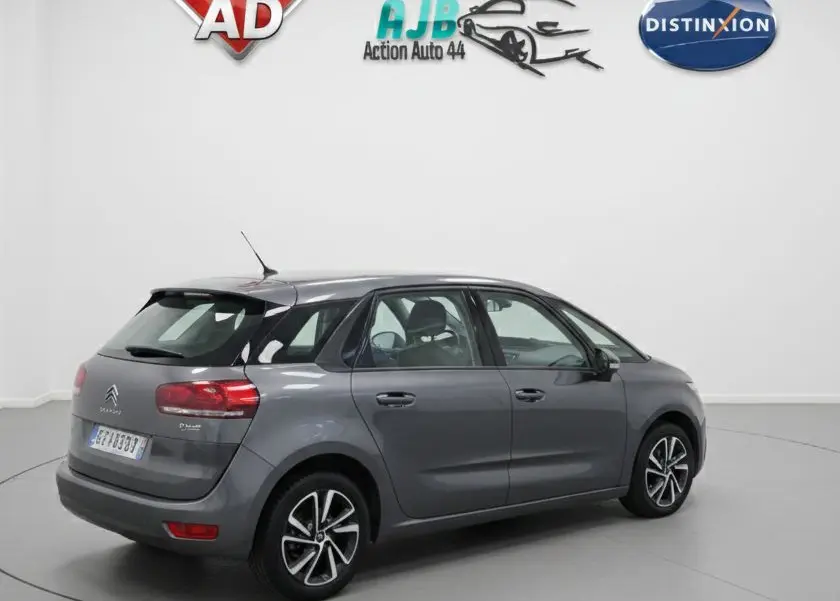 Vue 3/4 arrière gauche d'une Citroën C4 Picasso marron 2017 avec porte avant gauche ouverte sur parking humide.