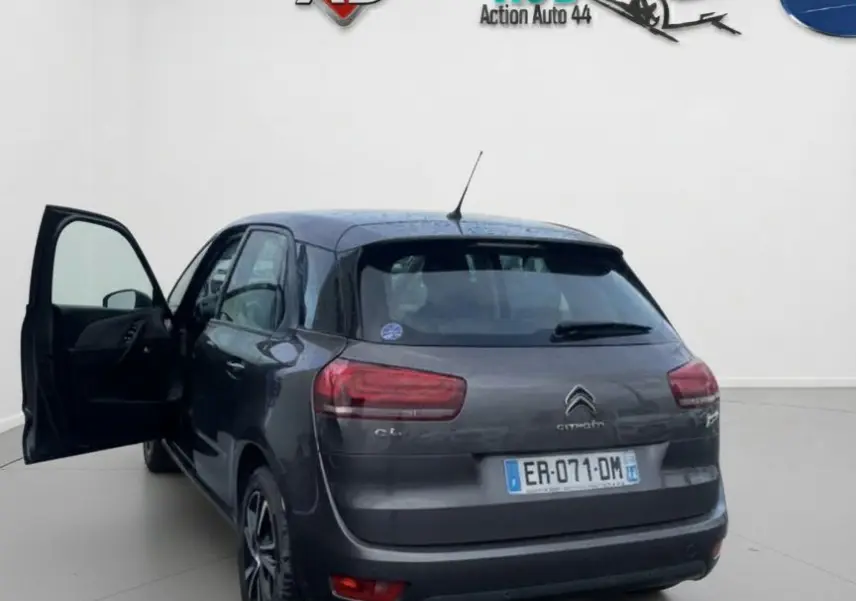 Vue de profil côté gauche d'une Citroën C4 Picasso marron avec porte avant ouverte et jantes alu sur sol humide.