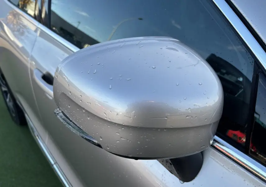 Rétroviseur côté gauche argent crépuscule métallisé du Volvo XC60 2024 avec gouttes d'eau et encadrement chromé.