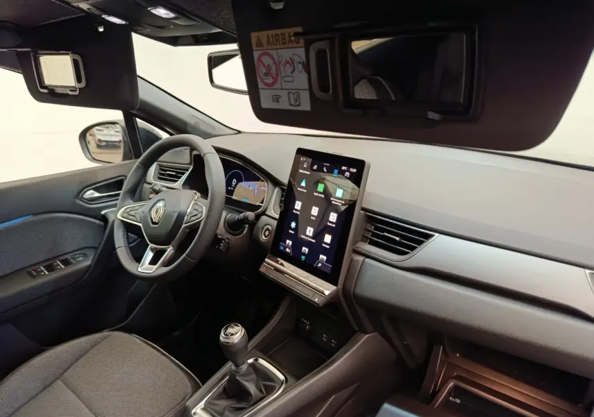 Vue intérieure côté conducteur du Renault Captur 2025, avec volant multifonctions, écran tactile vertical et levier de vitesse manuel.