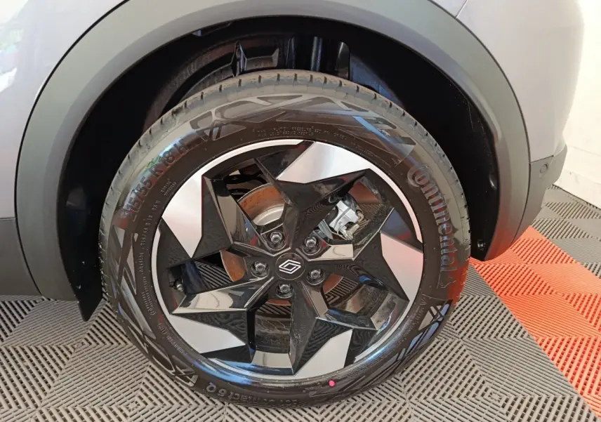 Gros plan sur la roue avant droite du Renault Captur gris foncé, mettant en valeur la jante noire et argentée au design géométrique.