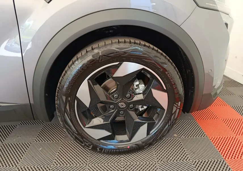 Gros plan sur la roue avant droite d'un Renault Captur gris foncé avec jante noire et argent au design géométrique.