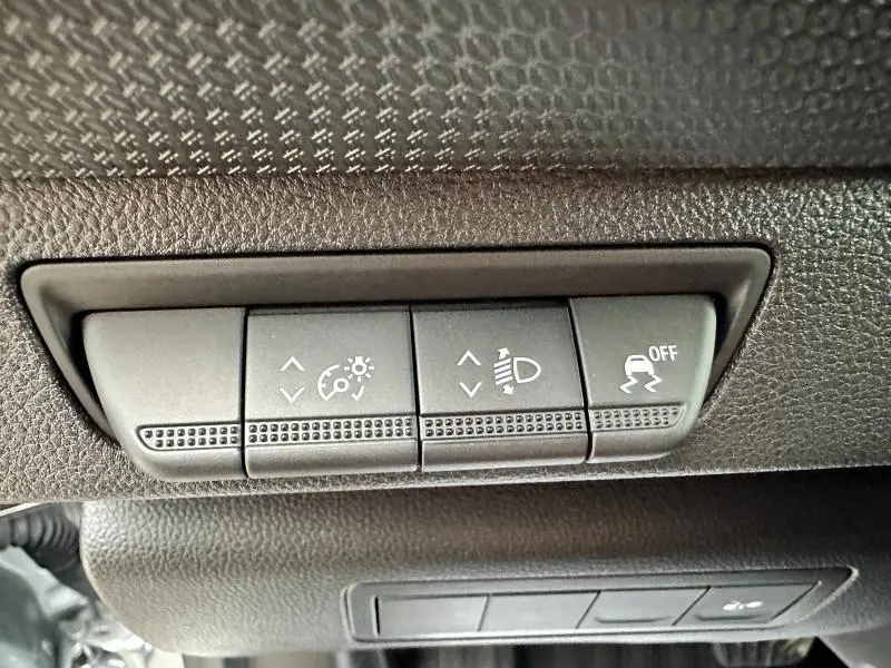 Gros plan sur les commandes de réglage des phares et de l'ESP dans l'habitacle noir du Nissan Townstar gris 2024.