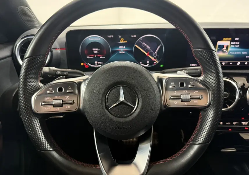 Vue rapprochée du volant cuir noir avec surpiqûres rouges et tableau de bord numérique d’une Mercedes Classe A AMG Line 2021.