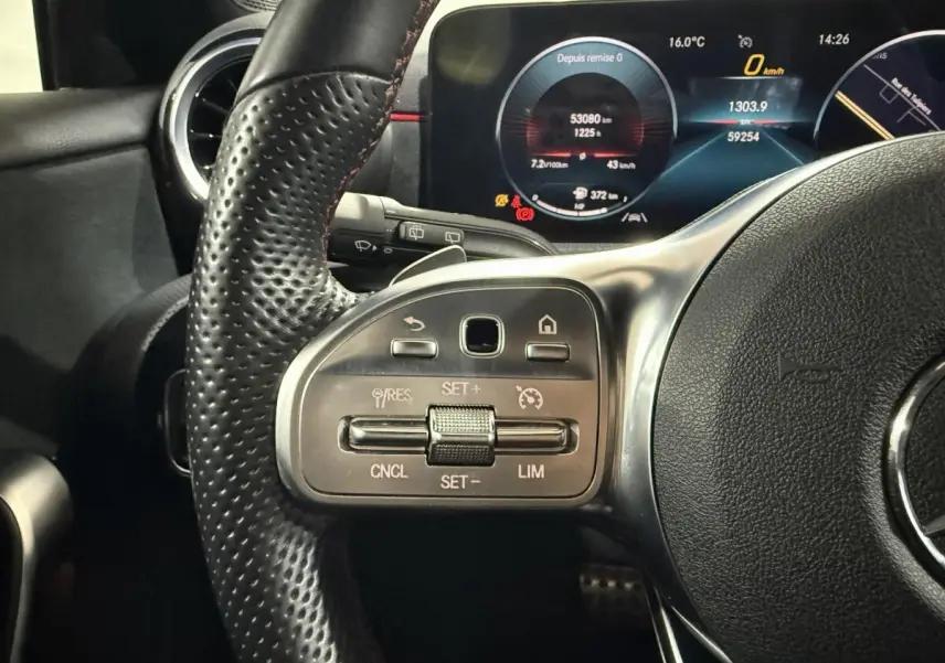Gros plan sur le volant cuir perforé côté gauche d’une Mercedes Classe A 200 AMG Line 2021 avec tableau de bord numérique allumé.