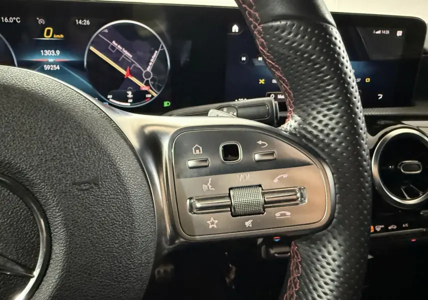 Gros plan sur le volant cuir perforé avec surpiqûres rouges et tableau de bord numérique de la Mercedes Classe A AMG Line gris foncé.