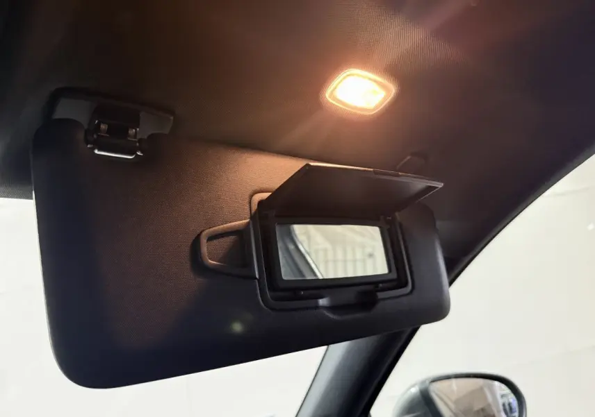 Gros plan sur le pare-soleil côté conducteur avec miroir ouvert et éclairage intérieur allumé dans une Mercedes Classe A gris foncé.