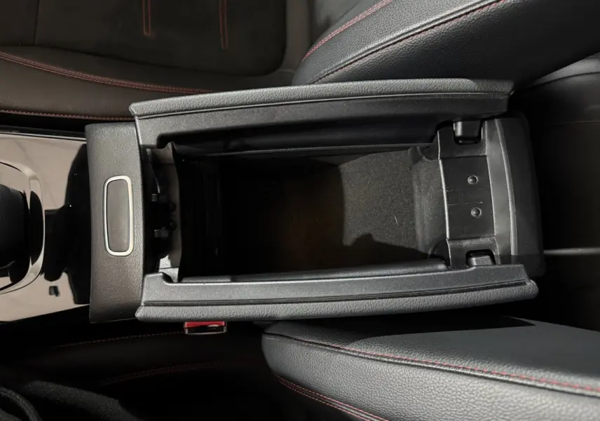 Vue plongeante sur la console centrale noire avec rangement ouvert et surpiqûres rouges des sièges cuir d’une Mercedes Classe A AMG Line.
