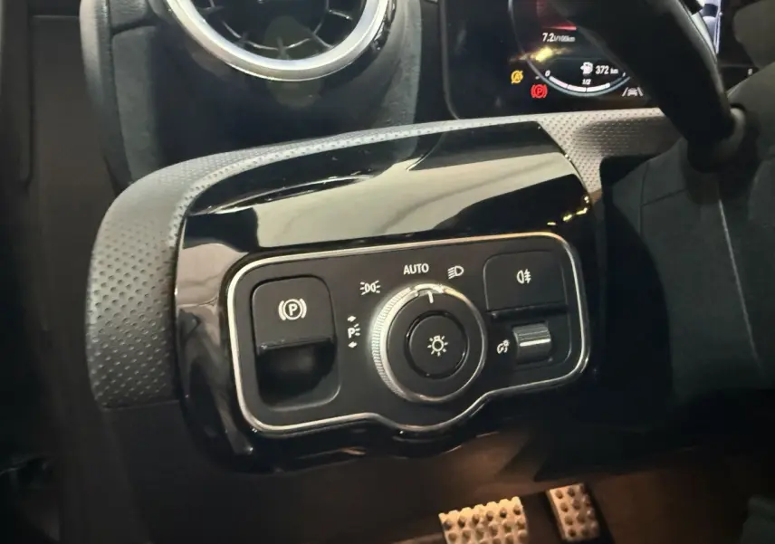 Gros plan sur le panneau de commande des phares et frein à main électrique, intérieur noir d'une Mercedes Classe A AMG Line 2021.