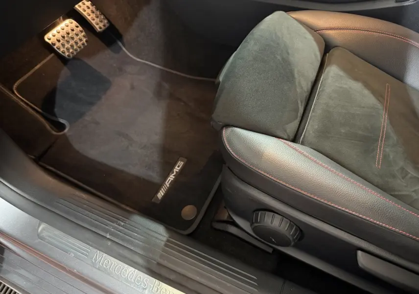 Vue rapprochée du siège conducteur cuir noir avec surpiqûres rouges et tapis AMG sur sol noir d'une Mercedes Classe A gris foncé.