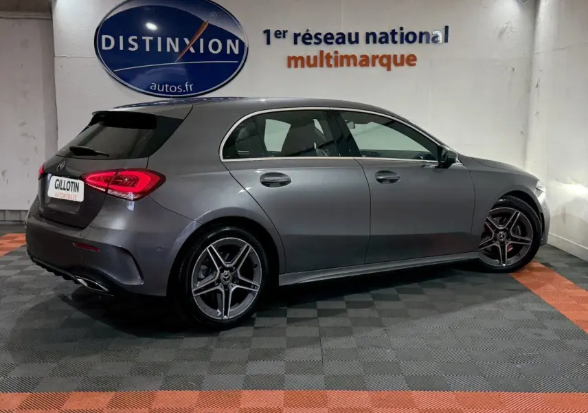 Vue latérale droite d'une Mercedes Classe A 200 AMG Line gris foncé en intérieur, avec jantes alliage et feux arrière LED allumés.
