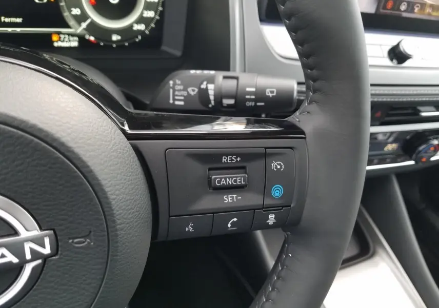 Gros plan sur le volant noir du Nissan Qashqai 2025, avec commandes de régulateur de vitesse et tableau de bord numérique en arrière-plan.