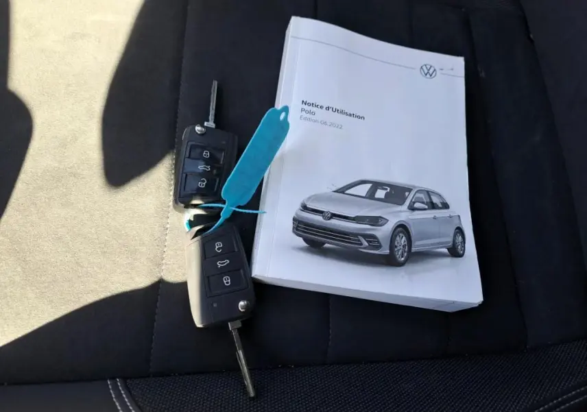 Notice d'utilisation Volkswagen Polo gris 3/4 avant sur siège noir avec deux clés de voiture posées à côté.