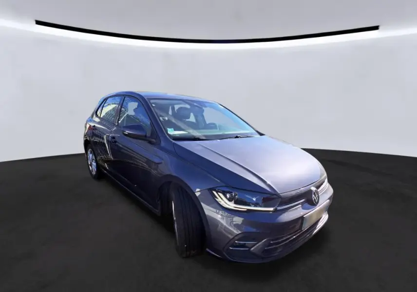 Volkswagen Polo gris vue 3/4 avant droit, avec projecteurs LED et calandre chromée visible.