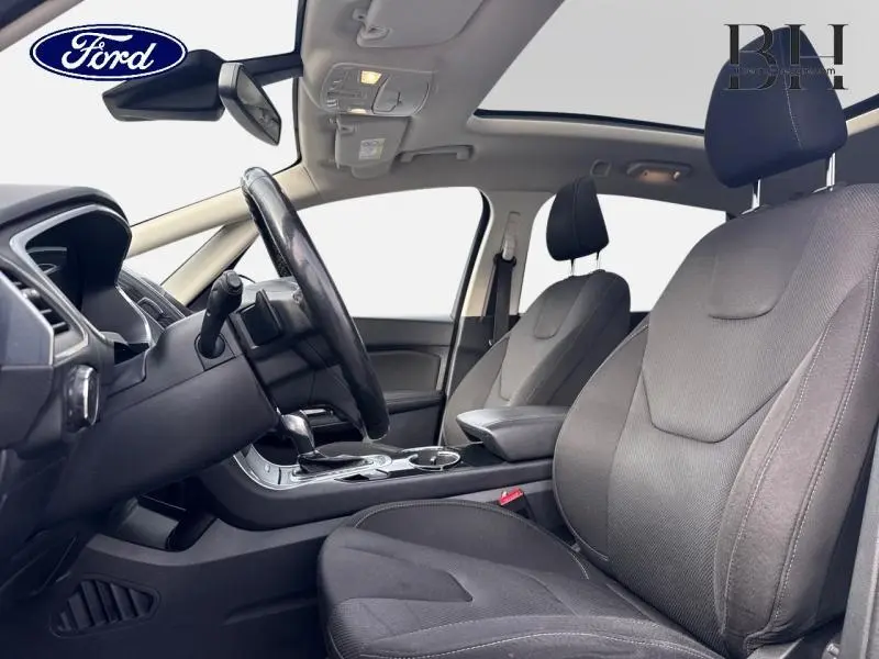 Vue intérieure côté conducteur du Ford S-MAX 2018 avec sièges tissu noir et toit panoramique en verre.