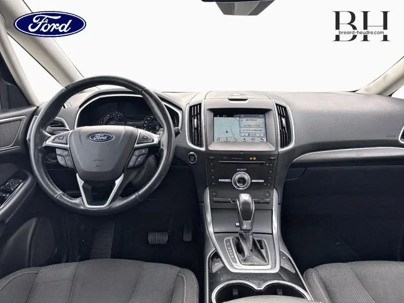 Vue intérieure avant du Ford S-MAX 2018 avec tableau de bord noir, écran tactile central et volant cuir multifonctions.