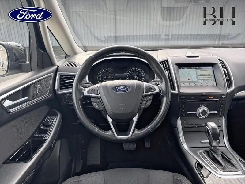 Vue intérieure frontale du poste de conduite du Ford S-MAX noir, avec volant multifonction et écran tactile GPS.