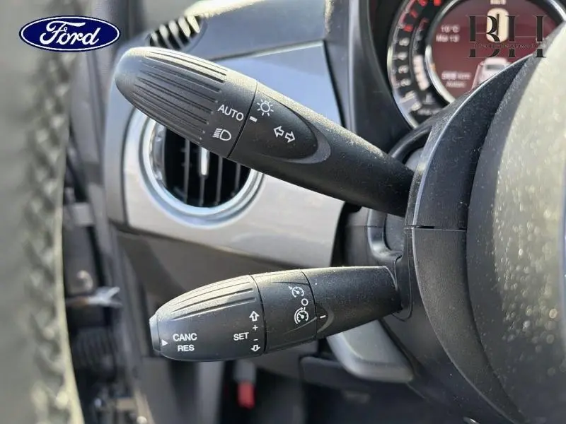 Détail des commandes au volant noir de la FIAT 500 Electroclash Grey, avec indicateurs et régulateur de vitesse visibles.
