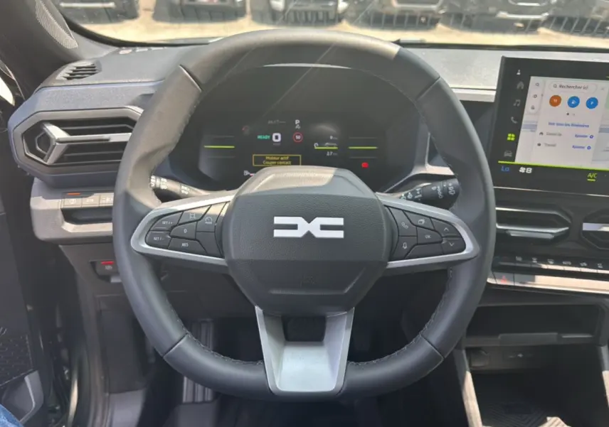 Vue intérieure centrée sur le volant cuir noir du Dacia Duster HEV 140 Journey Plus avec tableau de bord digital et écran tactile.