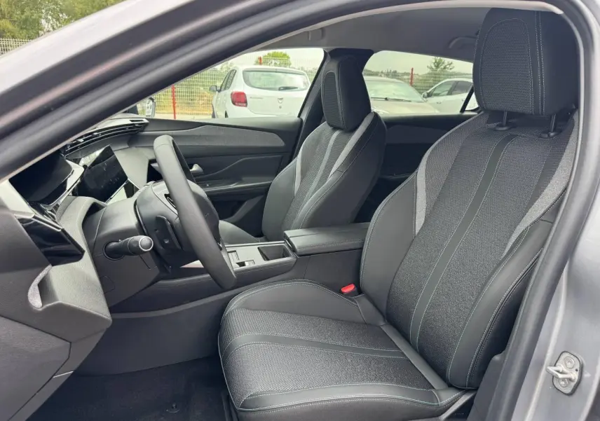Vue intérieure côté conducteur de la Peugeot 308 1.2 Hybrid 145ch Allure gris Artense, sièges tissu et cuir noir avec surpiqûres.