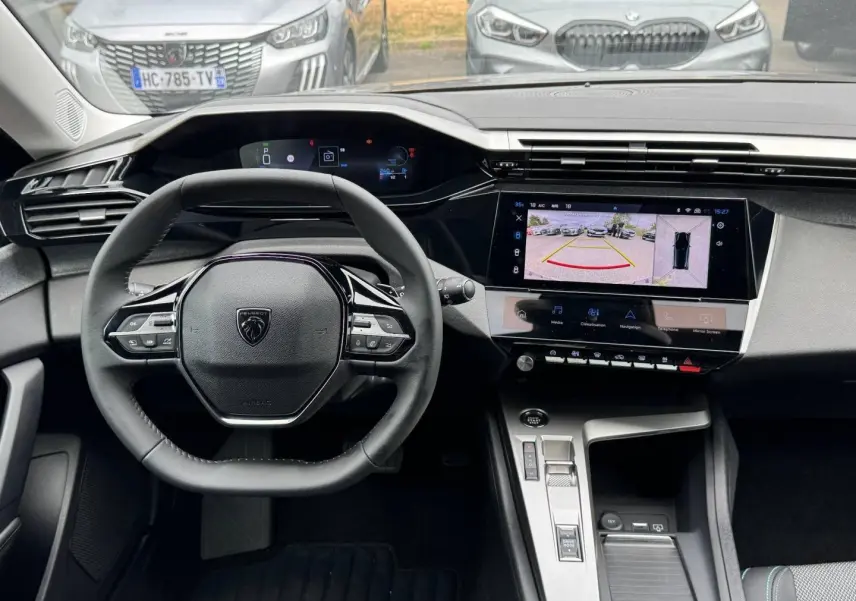 Vue intérieure centrée sur le volant Peugeot 308 gris Artense, avec tableau de bord numérique et écran tactile affichant la caméra de recul.