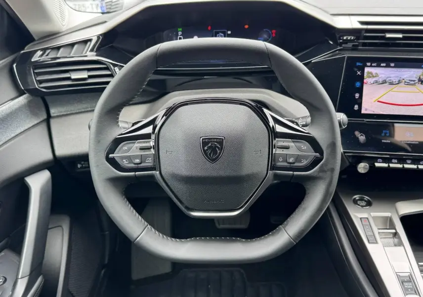 Vue rapprochée du volant multifonction Peugeot 308 2025 avec tableau de bord numérique et écran tactile de caméra de recul.
