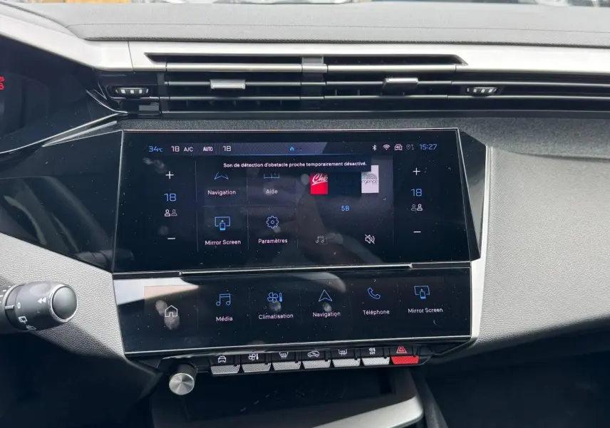 Vue rapprochée de l’écran tactile central multifonction de la Peugeot 308 gris Artense, avec commandes digitales et boutons physiques.