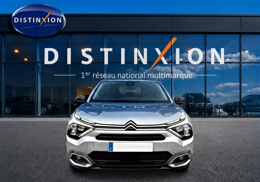 Citroën C4 gris vue de face, avec phares LED distinctifs, garée devant une vitrine Distinxion.