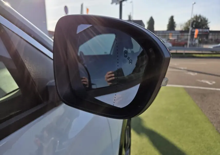 Rétroviseur extérieur droit noir sur Renault Austral blanc nacré, avec détection d'angle mort visible au soleil.