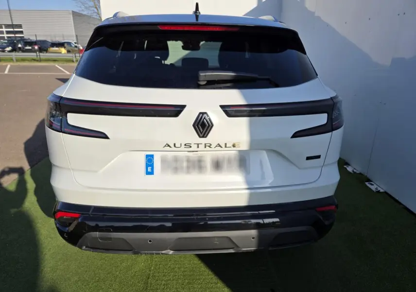 Vue arrière d'un Renault Austral blanc nacré avec toit noir, feux arrière horizontaux et logo central visible.