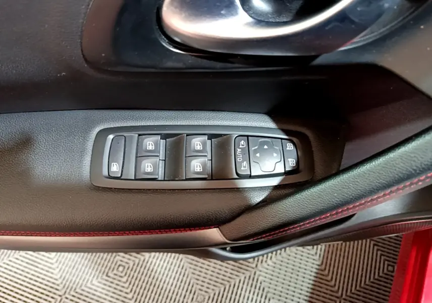 Gros plan sur les commandes de lève-vitres et rétroviseurs côté conducteur du Renault Kadjar rouge, intérieur noir avec surpiqûres rouges.