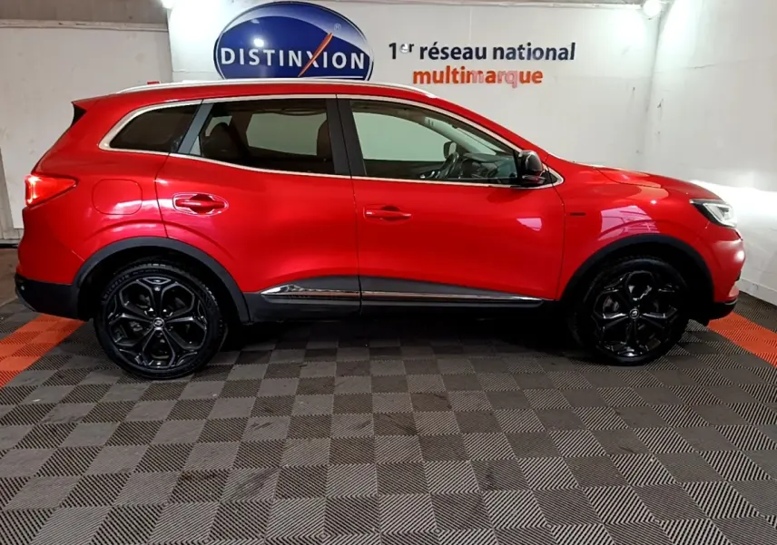 Profil droit d’un Renault Kadjar rouge SL Black Edition avec jantes noires et détails chromés, en intérieur showroom.