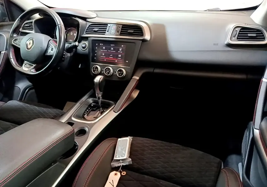 Vue intérieure côté conducteur du Renault Kadjar 2019, tableau de bord noir avec écran tactile et sellerie noire à surpiqûres rouges.