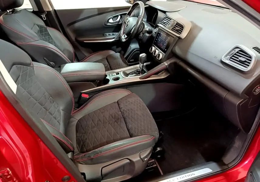 Vue intérieure côté conducteur du Renault Kadjar rouge, sièges noirs avec surpiqûres rouges et console centrale avec écran tactile.
