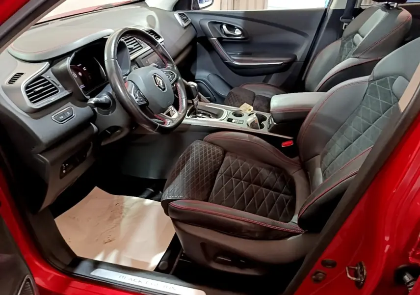 Vue intérieure côté conducteur du Renault Kadjar SL Black Edition rouge, mettant en valeur le volant cuir et les sièges noirs avec surpiqûres rouges.